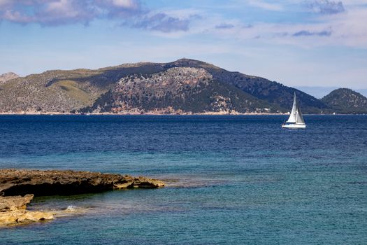Bay on the peninsula La Victoria, Mallorca with ridge in the background, sailing boat, blue water and rocks in the sea