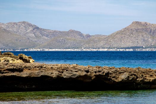 Bay on the peninsula La Victoria, Mallorca with ridge in the background, blue water and rocks in the sea