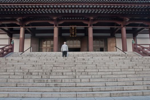 TOKYO, JAPAN - DECEMBER 1, 2018:  Zojo-ji Buddhist temple. This is a famous temple which has the oldest wooden main gate in Tokyo built from 1622. There is an old man stands to pray in front of the main temple hall.