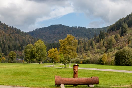 Landscape with wooden drinking fountain, green meadow, multi colored trees, mountain range with forest and blue sky with clouds  nearby Menzenschwand, Black Forest, Germany
