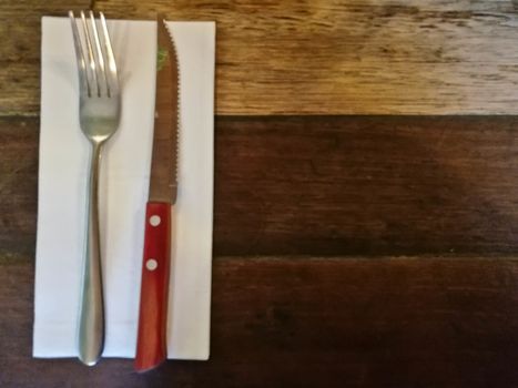 Top view of silver fork and knife on tissue paper on wooden classic table