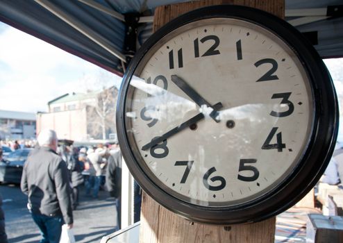 Analog old vintage classical white big clock with black rim and hands in Sunday flea market with crowds