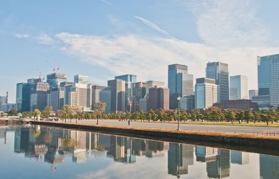 TOKYO, JAPAN - DECEMBER 1, 2018: Central Tokyo skyline of skyscraper office buildings in business and financial district. The calm pond shows a reflection of the buildings. There is a group of people stand near the pond.