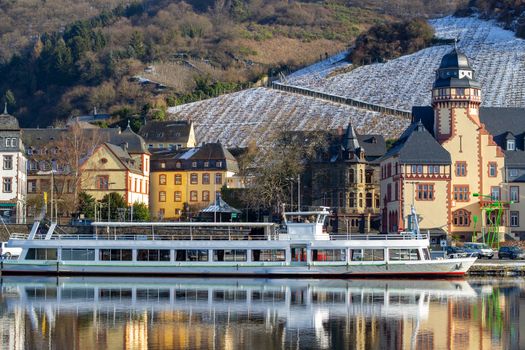 View at the valley of the river Moselle and the city of Bernkastel-Kues with passenger ship and vineyards with snow in the background
