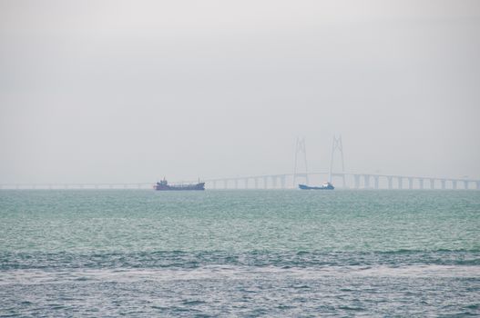 HONG KONG, HONG KONG SAR - NOVEMBER 18, 2018: Zuhai giantic mega bridge between China mainland and Hong Kong island. There are 2 ships floating near the bridge in hazy afternoon.