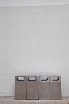 Four of different types of grey metal bins lays in front of white building wall