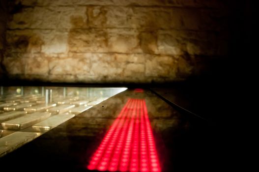 Many gold bars kept in the dark of a safe strong room with red LED light bar