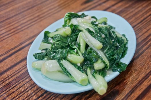 Fresh Chinese small cabbage choy sum stir-fried vegetable with oyster sauce and garlic served hot on a plate