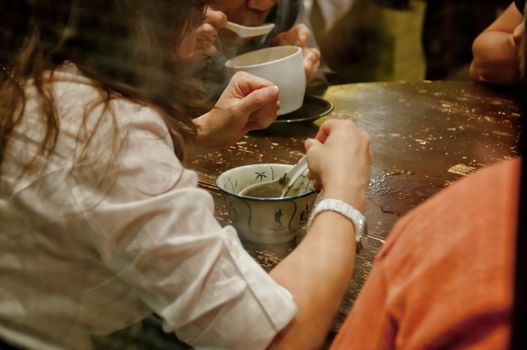 Lady sits and eats famous hot and cold sweet dessert soup in a round table with her friend in Hong Kong restaurant cafe