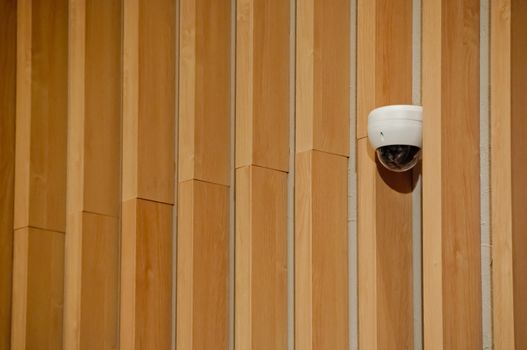 Modern white CCTV security camera dome  attached to wooden wall to safeguard wide area