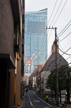 TOKYO, JAPAN - DECEMBER 1, 2018:  Long narrow alley toward modern big company headquarters corporate office in Tokyo. There are people walking on the side of the road in the morning.