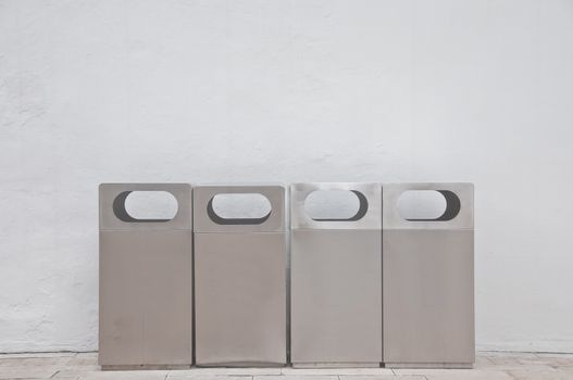 Four of different types of grey metal bins lays in front of white building wall