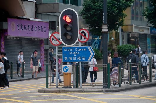 HONG KONG, HONG KONG SAR - NOVEMBER 18, 2018: Red person STOP traffic light in the city center above a sign to Airport Express station. There are many people in the photo.