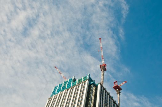 Underconstruction building in progress with many construction cranes and bright sunny blue sky with cloud