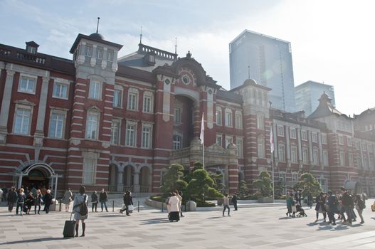 TOKYO, JAPAN - DECEMBER 1, 2018:  Tokyo Station railway building with warm sunlight shines to trees in late Autumn. There are many people walk on the street in front of the station.