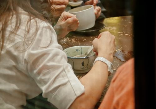 Lady sits and eats famous hot and cold sweet dessert soup in a round table with her friend in Hong Kong restaurant cafe