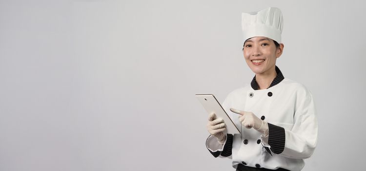 Asian woman chef holding smartphone or digital tablet and received food order from online shop or merchant application. she smiling in chef uniform and standing in studio with white color background.