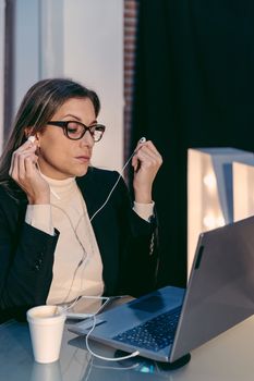 Adult female freelancer using laptop computer for listening music call while sitting in modern coffee shop interior, beautiful Caucasian woman working on net-book during coffee break in cafe bar