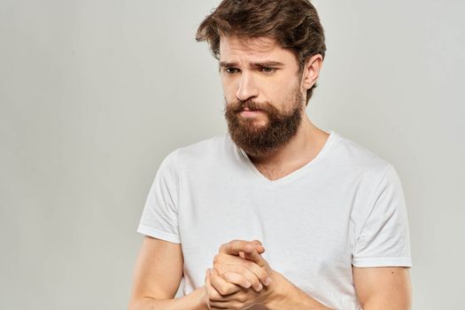 bearded man gesturing with his hands in a white t-shirt aggression light background. High quality photo