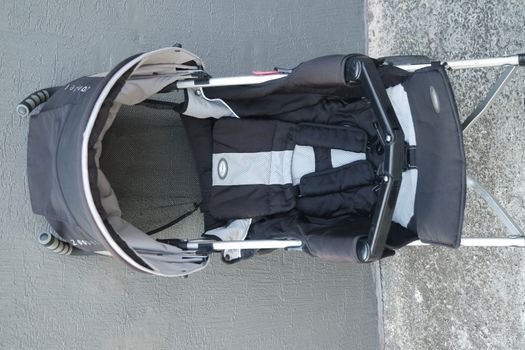 Black color baby stroller with head covering. Stroller is with concrete background