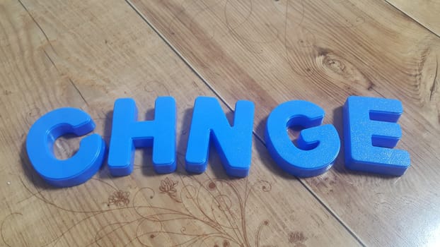 Plastic colored alphabets making words are placed on a wooden floor. These plastic letters can be used for teaching kids.