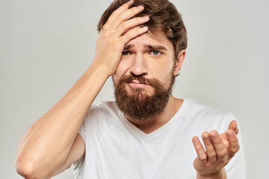 A man in a white t-shirt with a beard emotions displeased facial expression light background. High quality photo