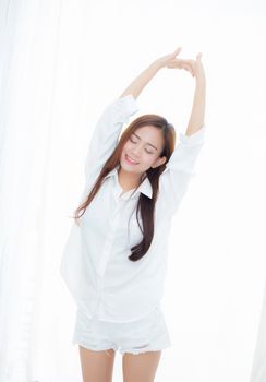 Beautiful young asian woman stretch and relax standing in bed after wake up morning at bedroom, new day and resting for wellness, lifestyle concept.