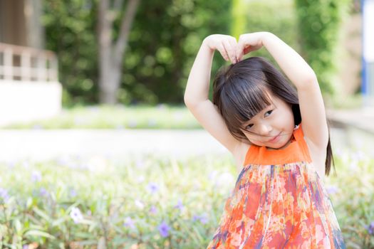 Beautiful portrait little girl asian of a smiling standing on green grass at the park, kid leisure and joyful in outdoor.