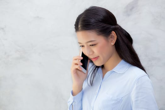 Beautiful young asian woman talking mobile phone and smile standing on cement background, freelancer female calling telephone, communication concept.