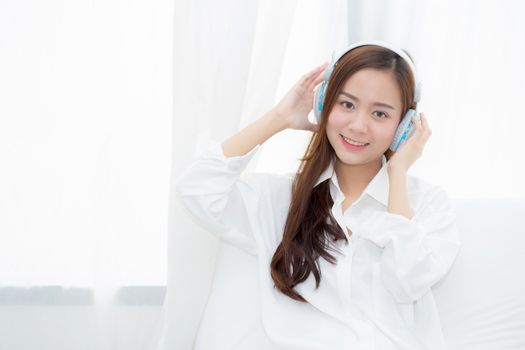 Beautiful asian young woman enjoy listen music with headphone while sitting in bedroom, relax girl with earphone internet online, leisure and technology concept.