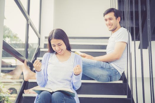 Couple asian handsome man and beautiful woman reading book and smile at home, boyfriend and girlfriend glad with activities together for leisure, education success concept.