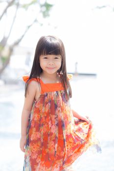 Beautiful portrait little girl asian of a smiling standing on green grass at the park, kid leisure and joyful in outdoor.