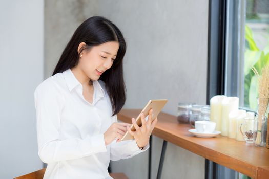 Beautiful portrait young asian woman using tablet computer in the coffee shop, businesswoman sitting looking tablet is work at cafe, communication concept.