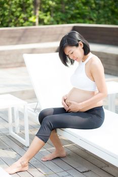 Portrait of beautiful pregnant asian young woman relax in the park, girl with belly sitting at swimming pool for wellness, tummy girl, health care concept.