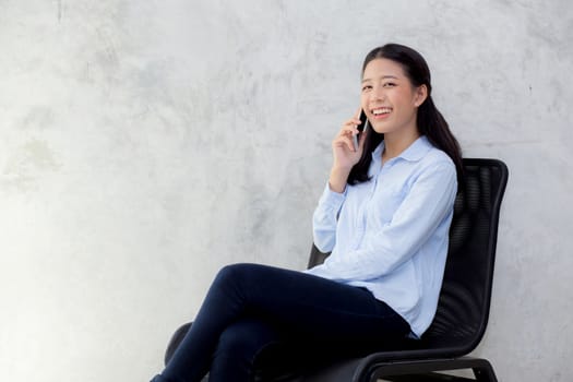 Beautiful young asian woman talking smart mobile phone and smile sitting on cement background, freelancer female calling telephone, communication concept.