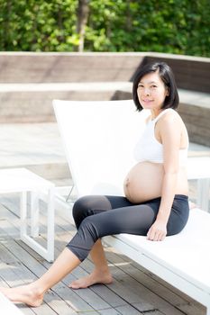 Portrait of beautiful pregnant asian young woman relax in the park, girl with belly sitting at swimming pool for wellness, tummy girl, health care concept.