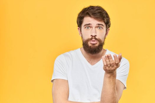 Bearded man in a white T-shirt gestures with his hands emotions studio yellow background. High quality photo