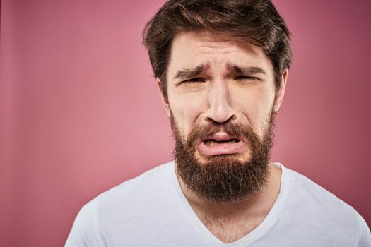 Emotional bearded man in white T-shirt discontent pink background. High quality photo