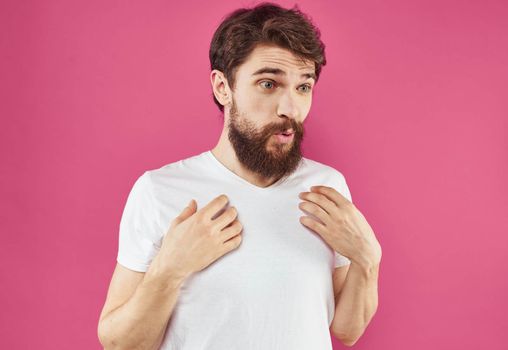 A cheerful guy with a beard laughs on a pink background and gestures with his hands. High quality photo