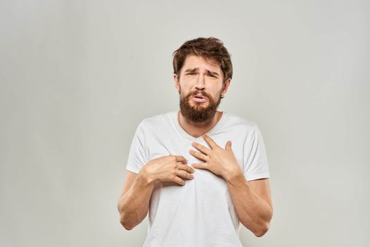 A man in a white t-shirt with a beard emotions displeased facial expression light background. High quality photo