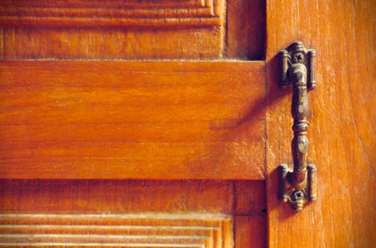 The vintage door handle on an old wooden door background and lighting and shadow in the morning. Closeup and copy space on the left. The concept of art and architecture in vintage style.