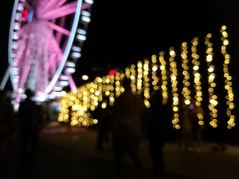 Defocused scene of giant pink flyer ferris wheel at night with yellow light fence and the crowd of people