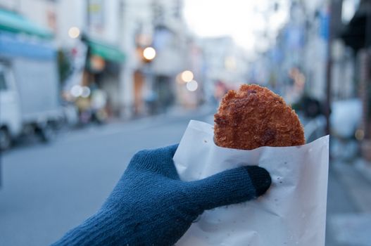 Left hand with glove holding deep fried chicken nugget piece in Winter