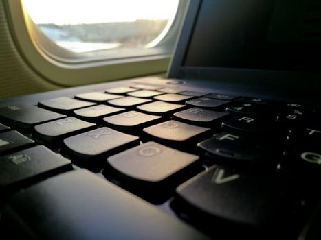 Laptop computer keyboard near airplane cabin window seat working on the go