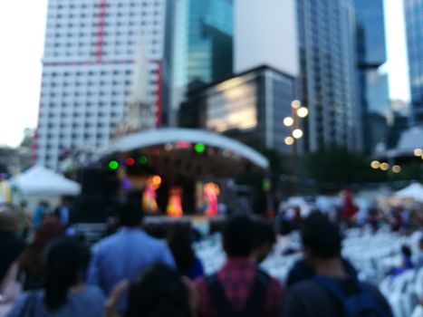 Defocused scene of crowd of people attending public concert celebrating New Year festival in city in Evening