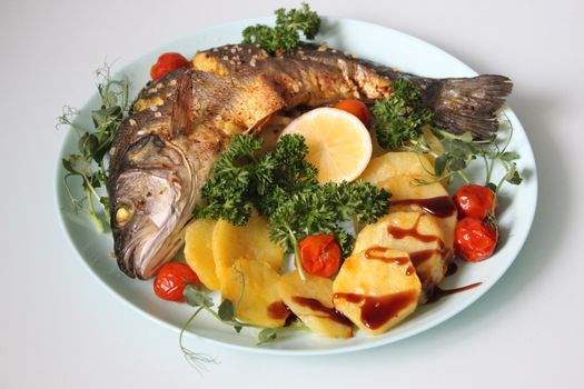 Fried fish with potatoes and decorated with lettuce and lemon on a light background.Texture or background