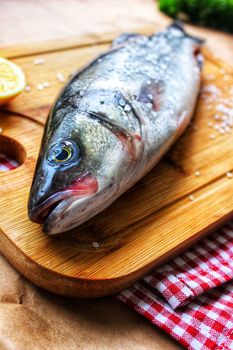 One raw fish on a wooden chopping Board is decorated with a lemon slice in close-up.Texture or background