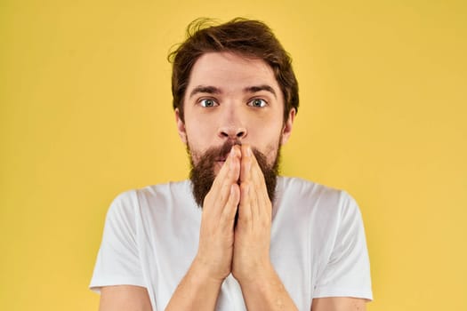 A man in a white t-shirt gestures with his hands lifestyle cropped view yellow background more fun. High quality photo