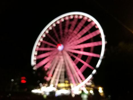 Defocused scene of giant pink flyer ferris wheel at night