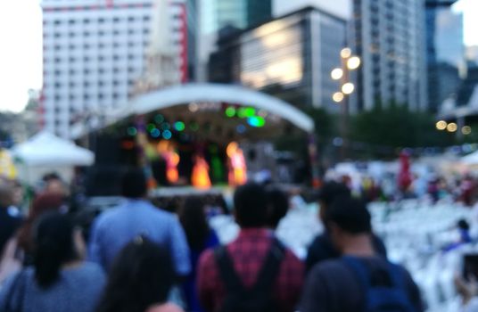 Defocused scene of crowd of people attending public concert celebrating New Year festival in city in Evening